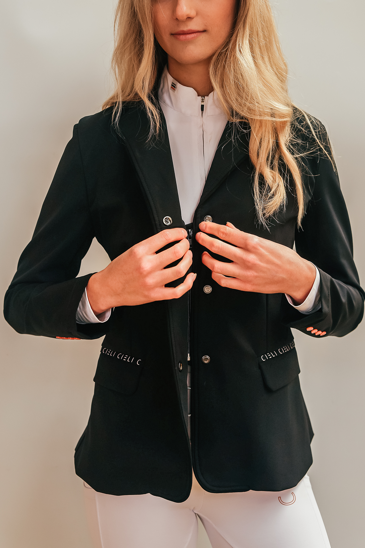 Blonde girl wearing Cieli Equestrian show jacket in black with orange details