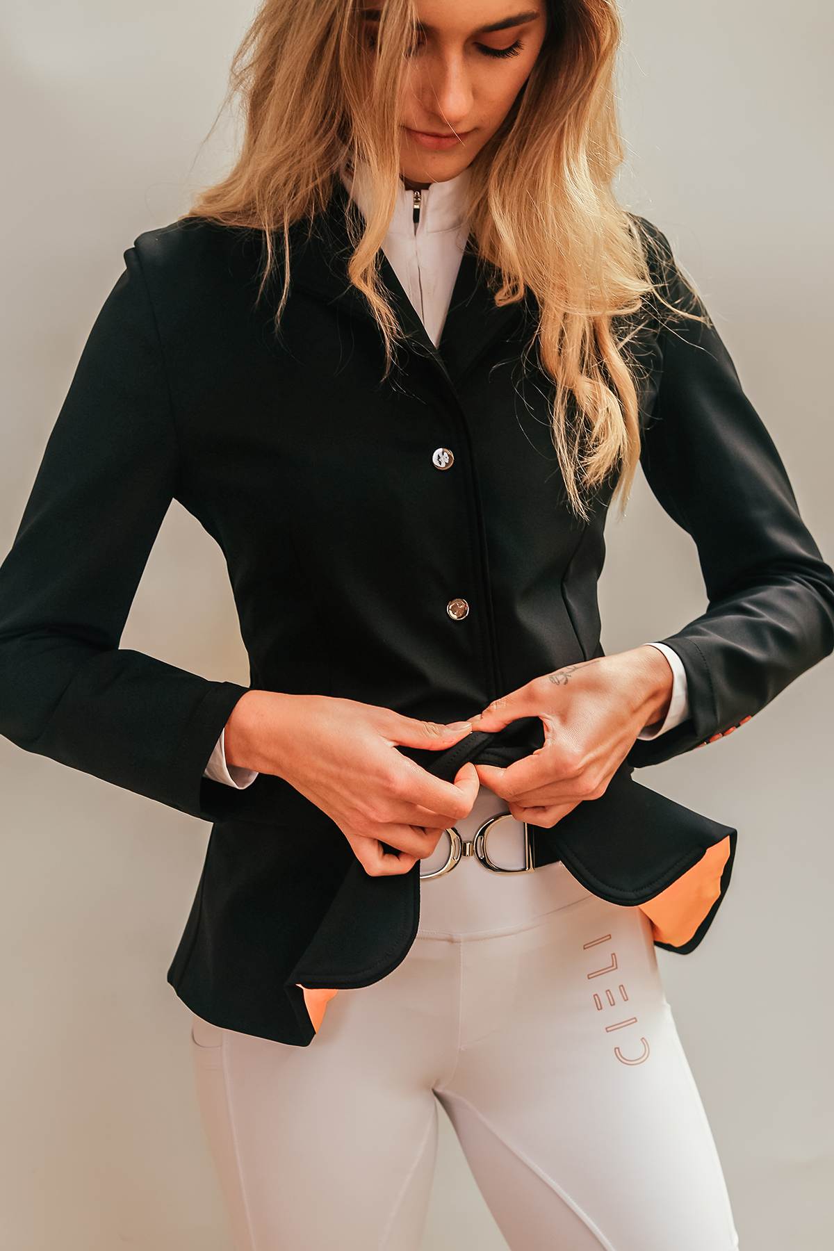 Blonde girl wearing Cieli Equestrian show jacket in black with orange details