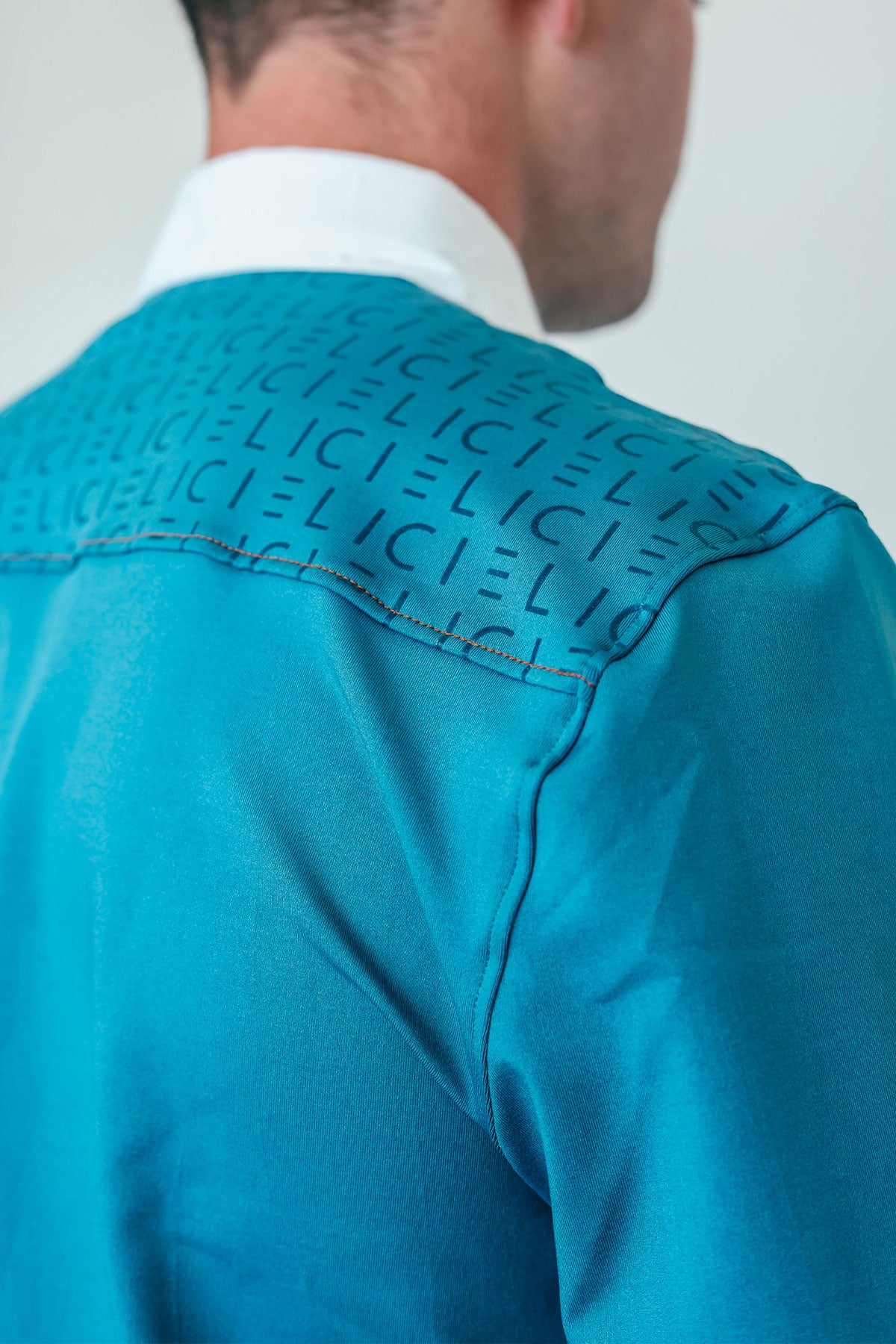Close-up of a turquoise shirt with 'CIELI' text on the shoulder against a plain background
