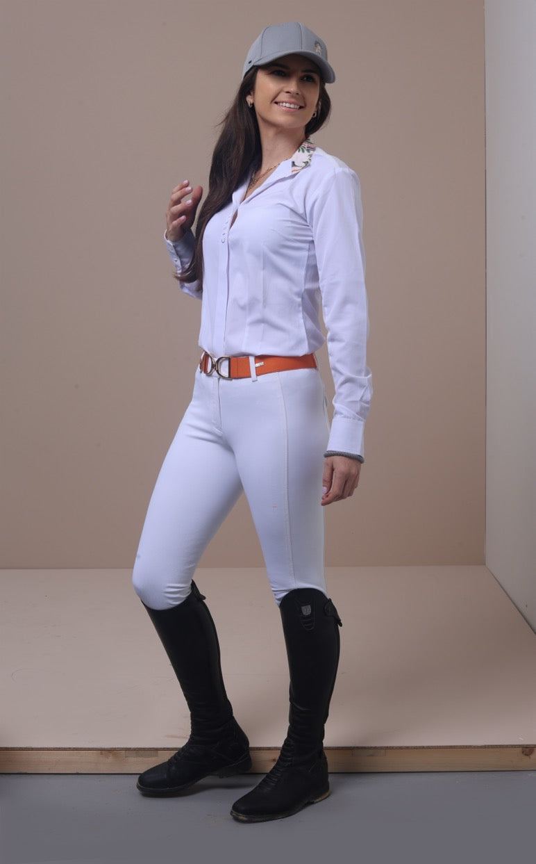 Woman in equestrian attire with white shirt, pants, and black boots against a plain background