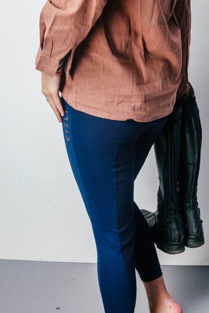Person wearing a brown shirt and blue leggings with black boots on a white background