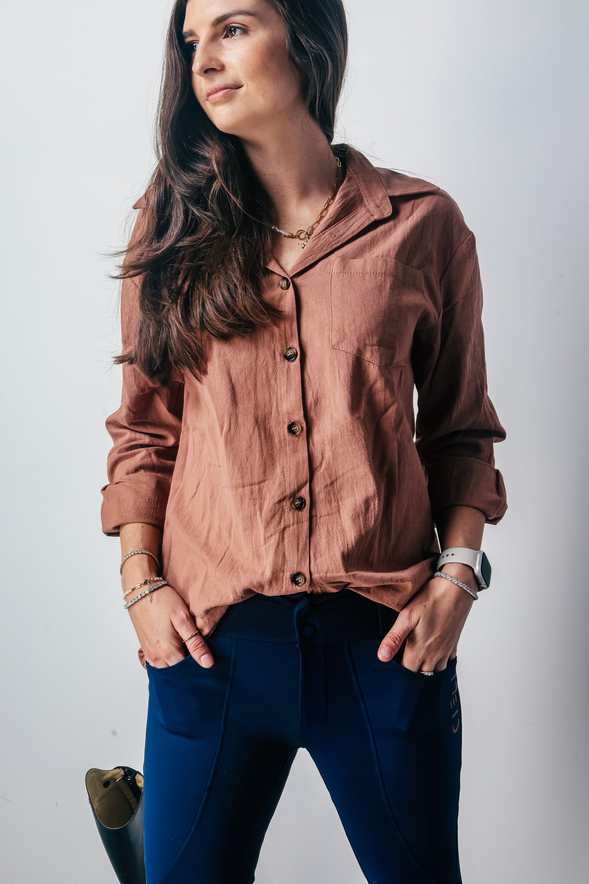 Woman wearing a brown button-up shirt and blue riding pants against a white background