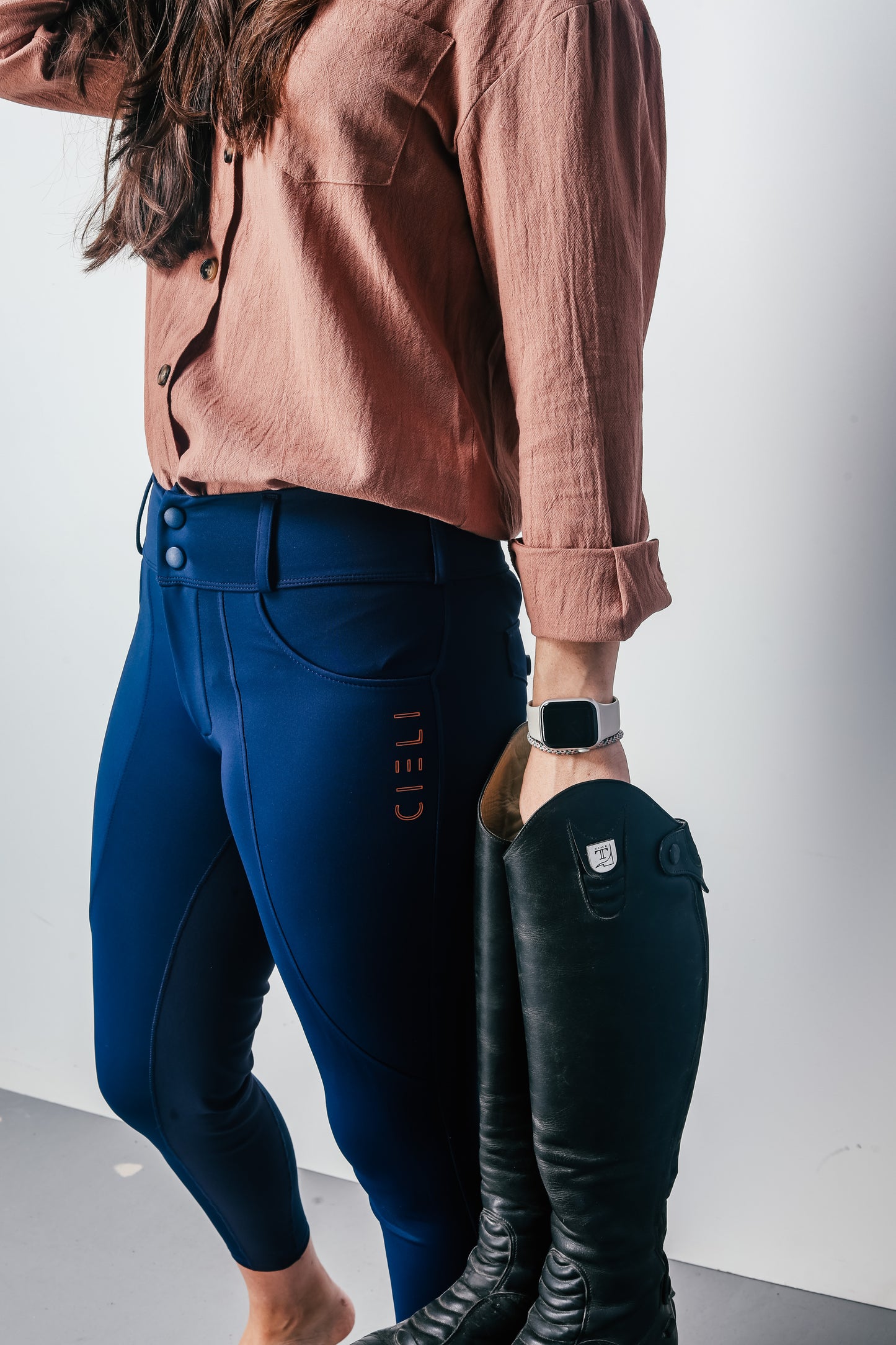 Person wearing blue riding pants with 'Ciel' branding and black riding boots on a white background