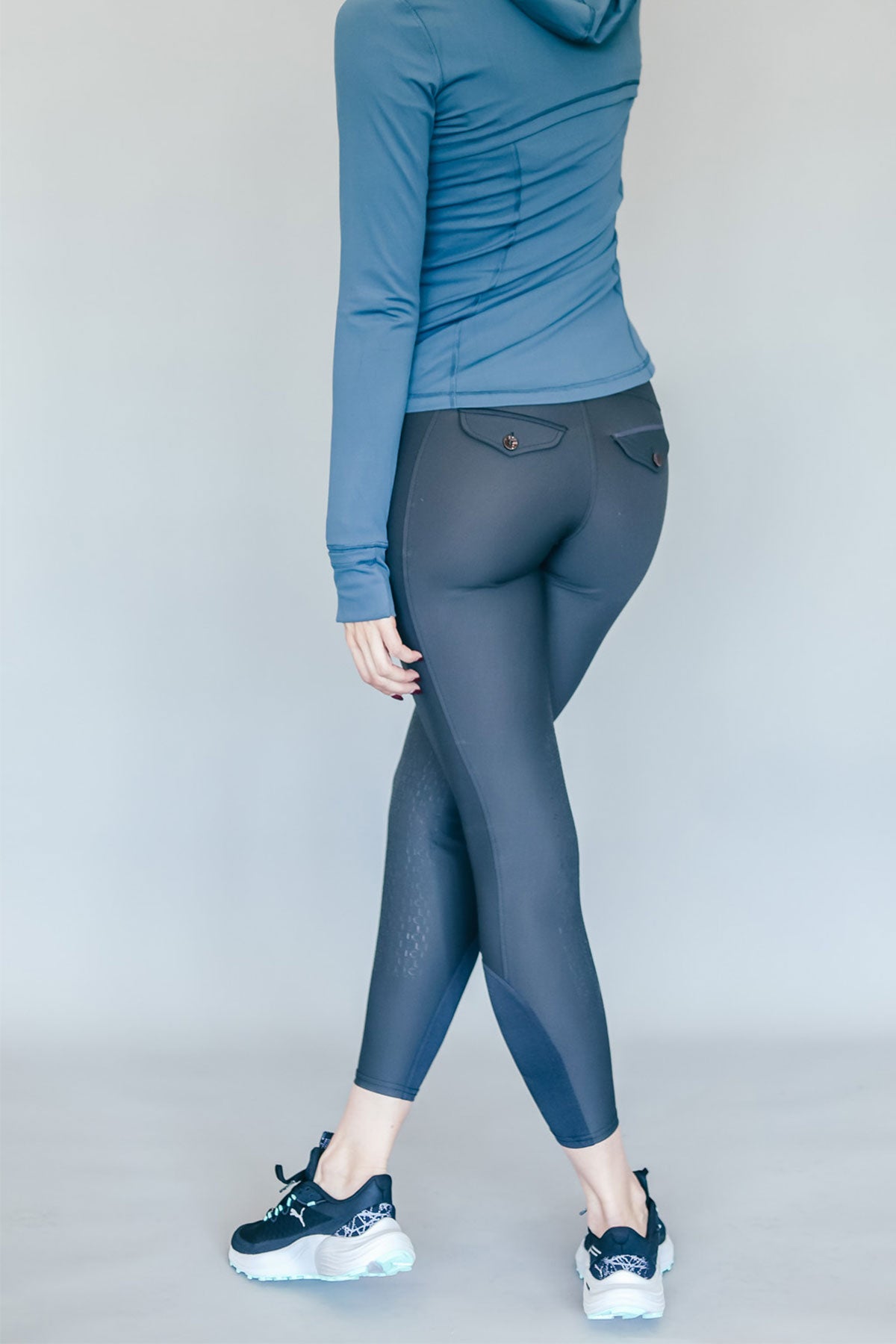 Person wearing a blue hoodie and gray riding pants on a plain background