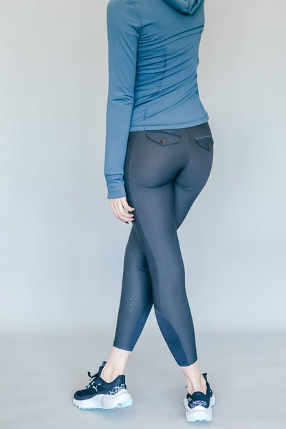 Person wearing a blue hoodie and gray riding pants on a plain background