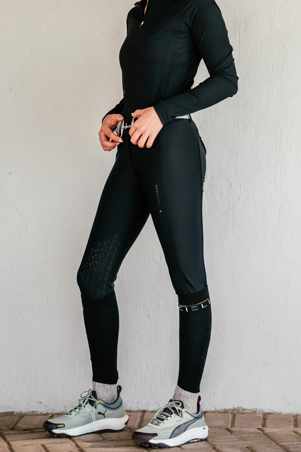 Person wearing black athletic riding pants and shoes against a white wall.