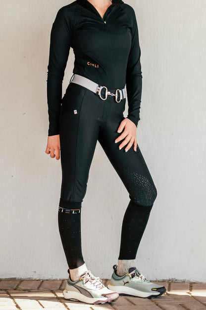 Person wearing a black shirt and riding pants with grey accents on a light background