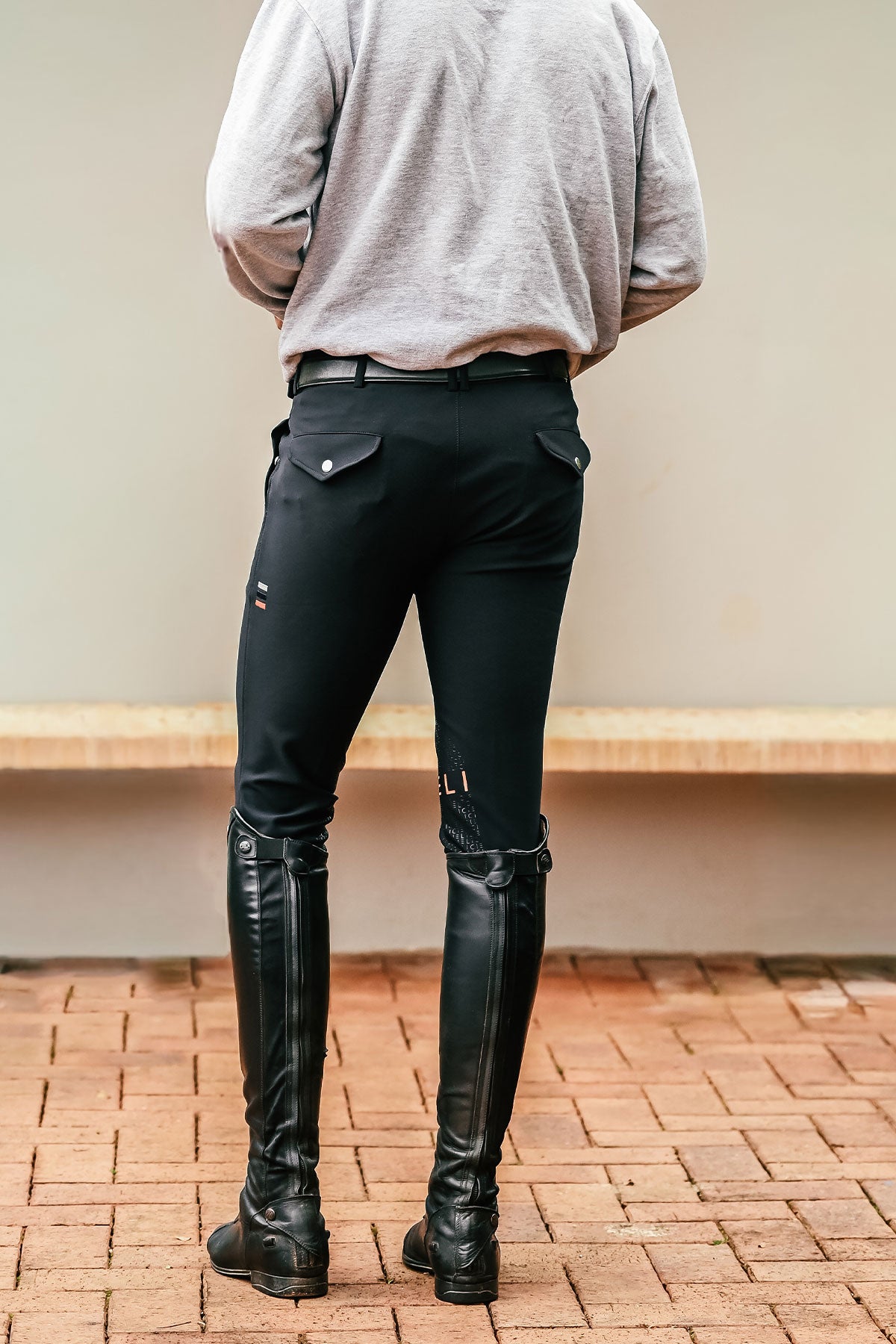 Person wearing black riding pants and boots on a brick floor.