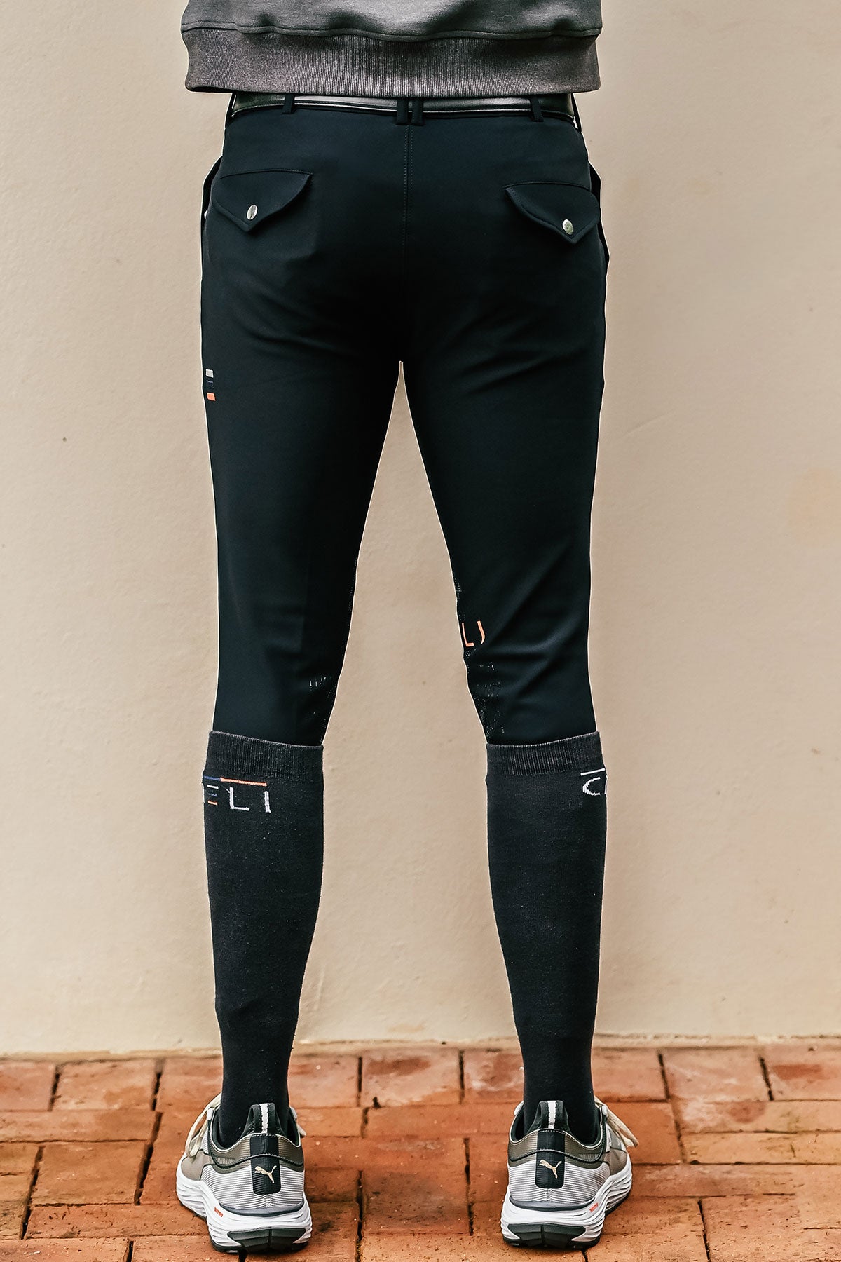 Person wearing black riding pants with a visible brand logo on a beige background