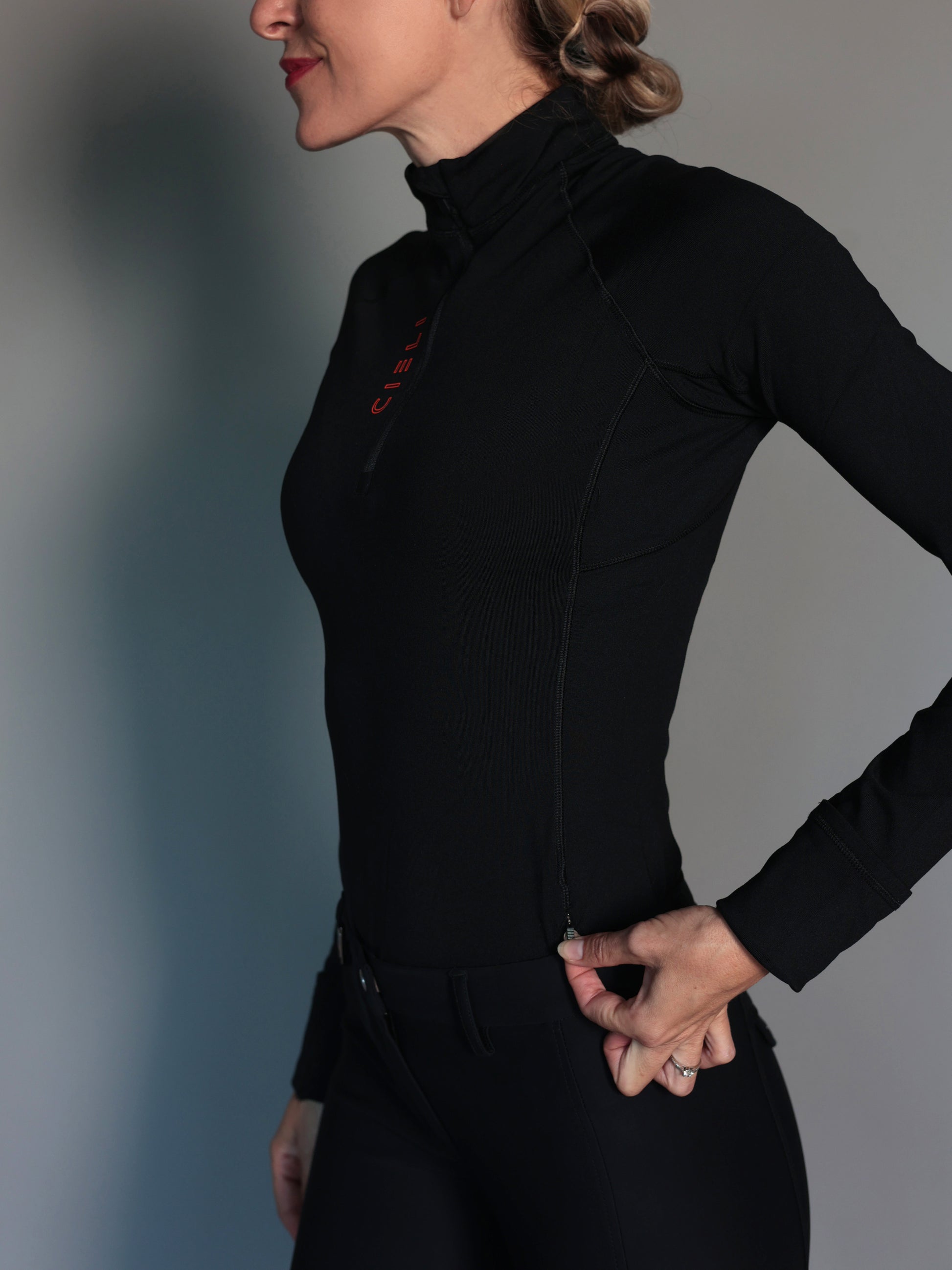 Person wearing an equestrian black long-sleeve top against a gray background