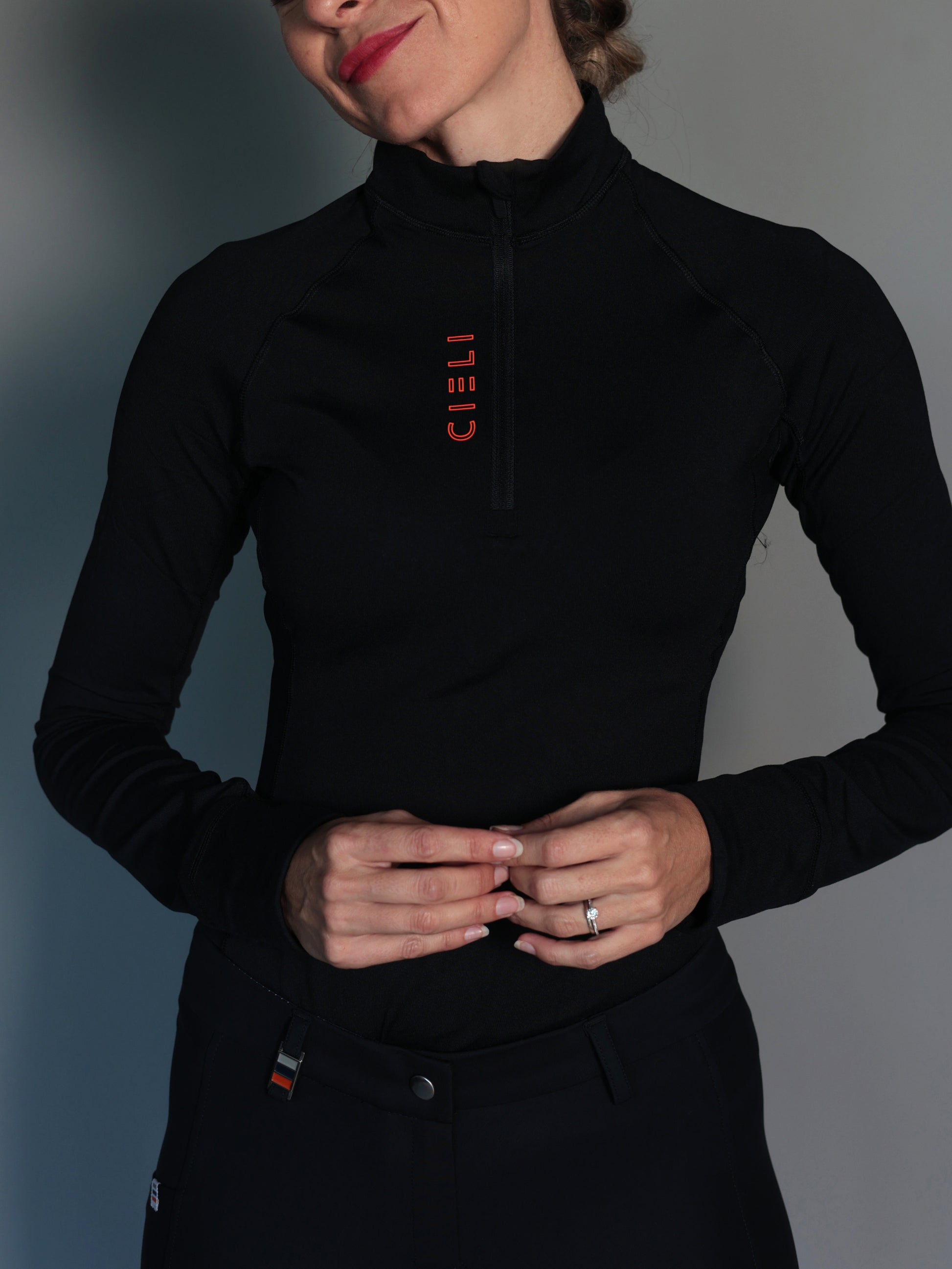 Person wearing an equestrian black high-necked top with a brand logo on a gray background