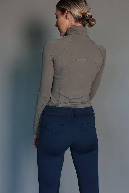 Person wearing a green long-sleeve top and blue breeches against a plain background