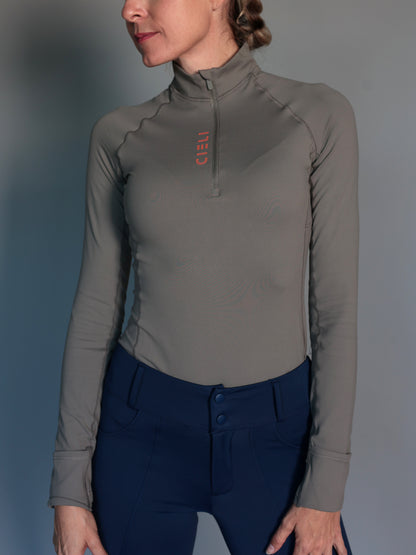 Person wearing a green equestrian long-sleeve top with a brand logo on a gray background