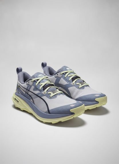 A pair of Puma running shoes in light gray and slate blue with pale yellow accents, displayed on a neutral light gray background.