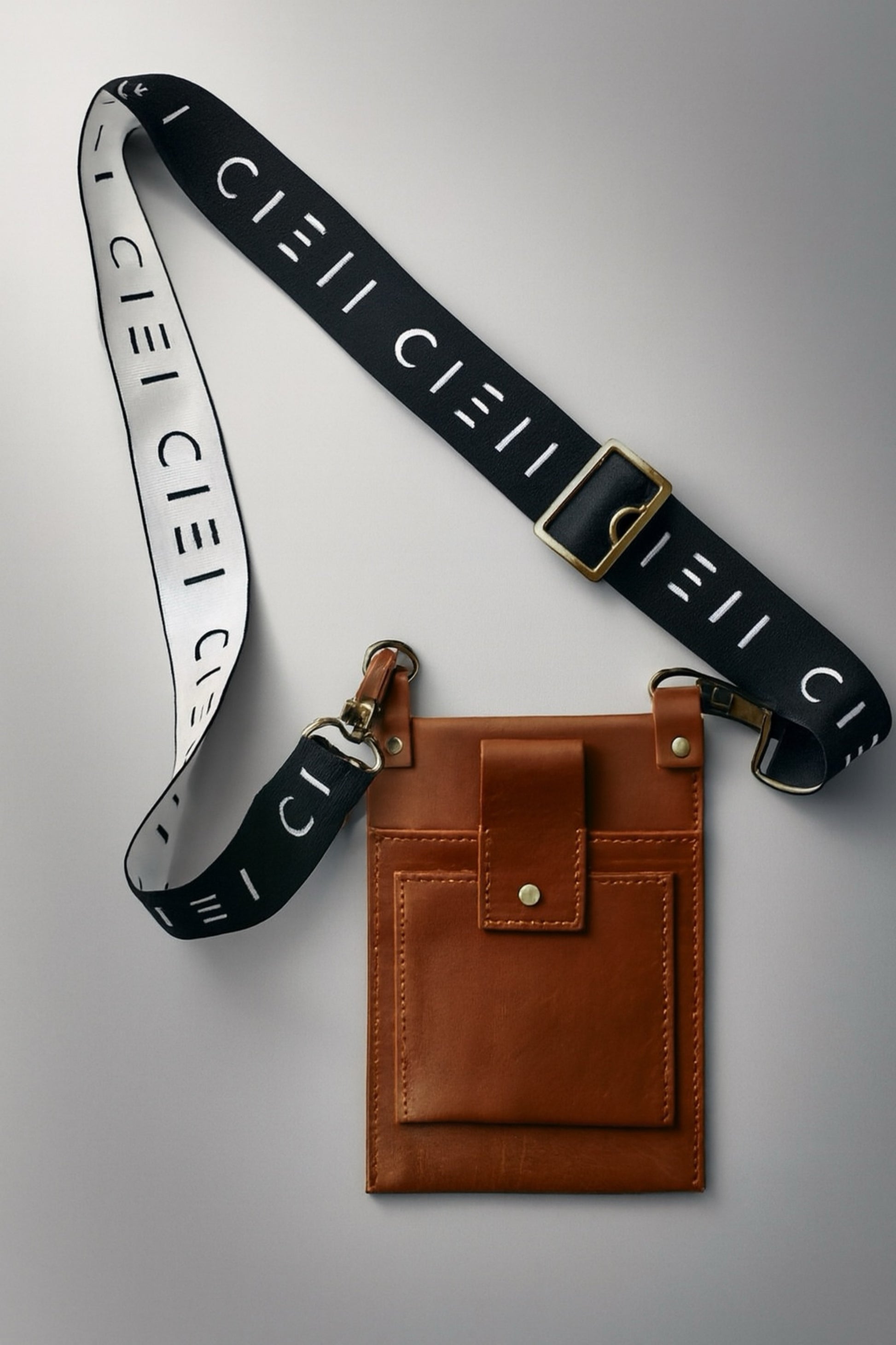 Black strap with gold hardware and white text, brown leather pouch on gray background
