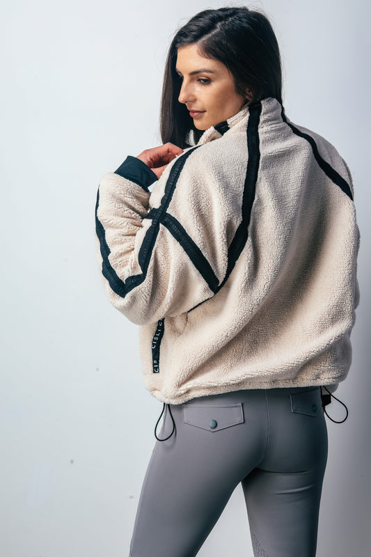 Woman wearing a beige fleece jacket with black accents on a white background