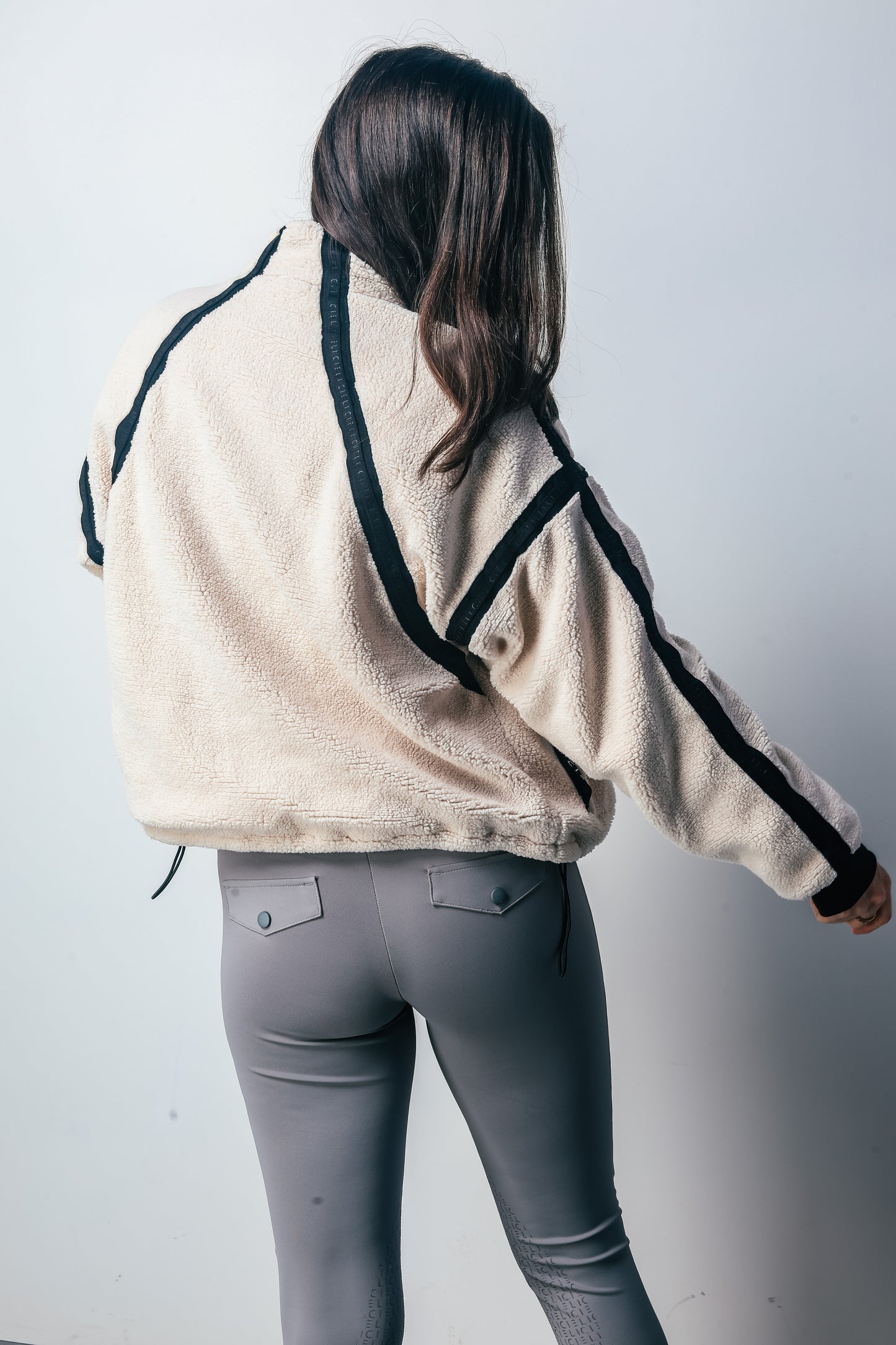 Person wearing a beige jacket with black accents and gray riding pants on a white background