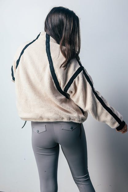 Person wearing a beige jacket with black accents and gray riding pants on a white background