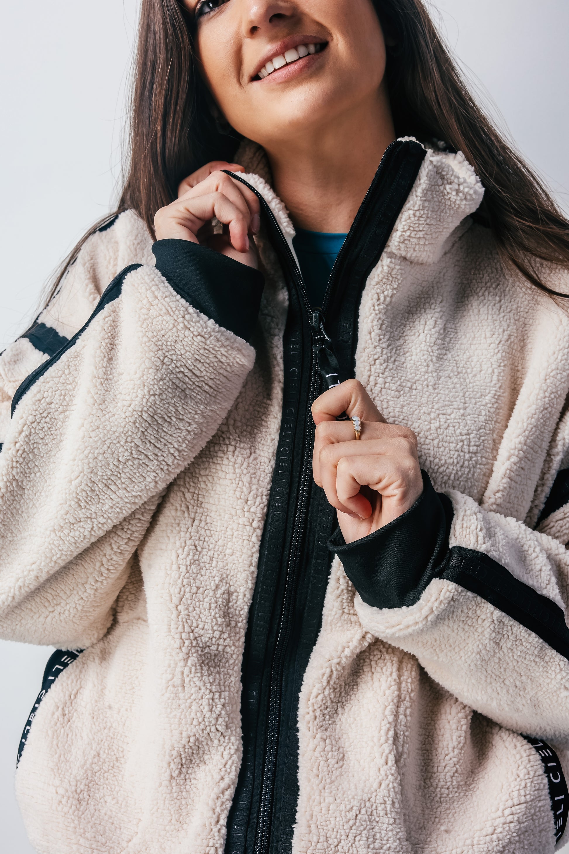 Woman wearing a beige fleece jacket with black accents on a white background
